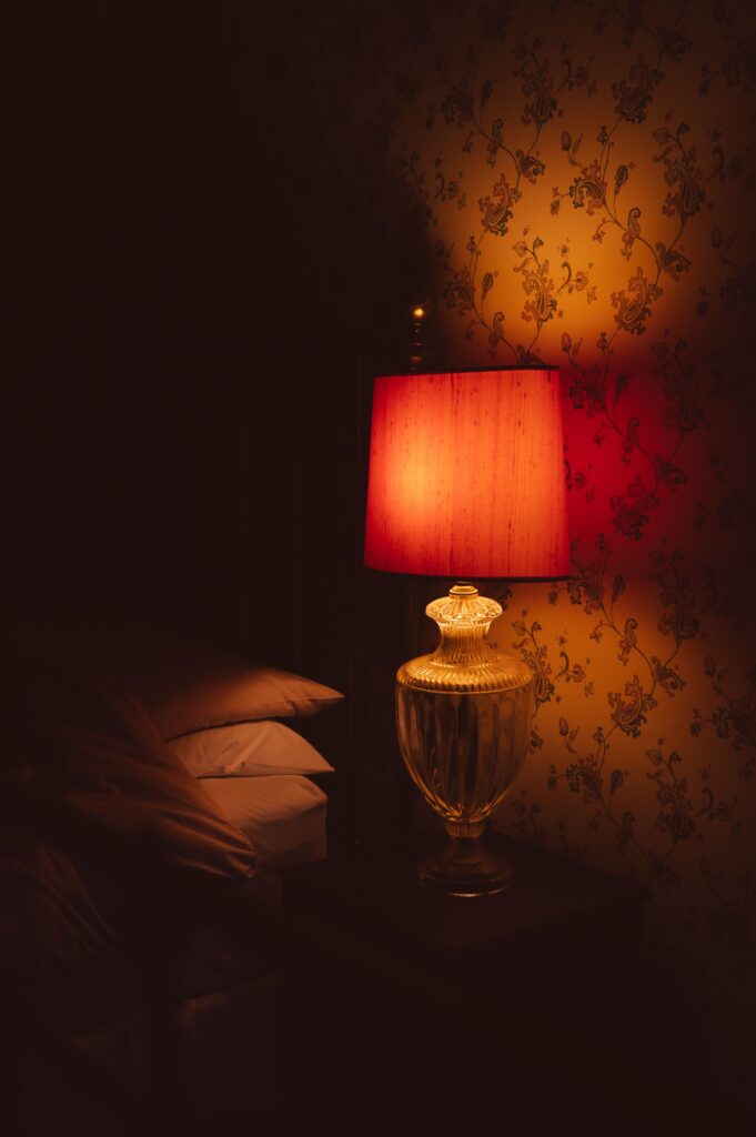 A cozy bedroom with a dim warm bedside lamp turned on